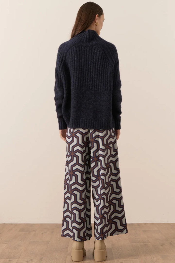 Person wearing a dark blue sweater and patterned pants against a beige background