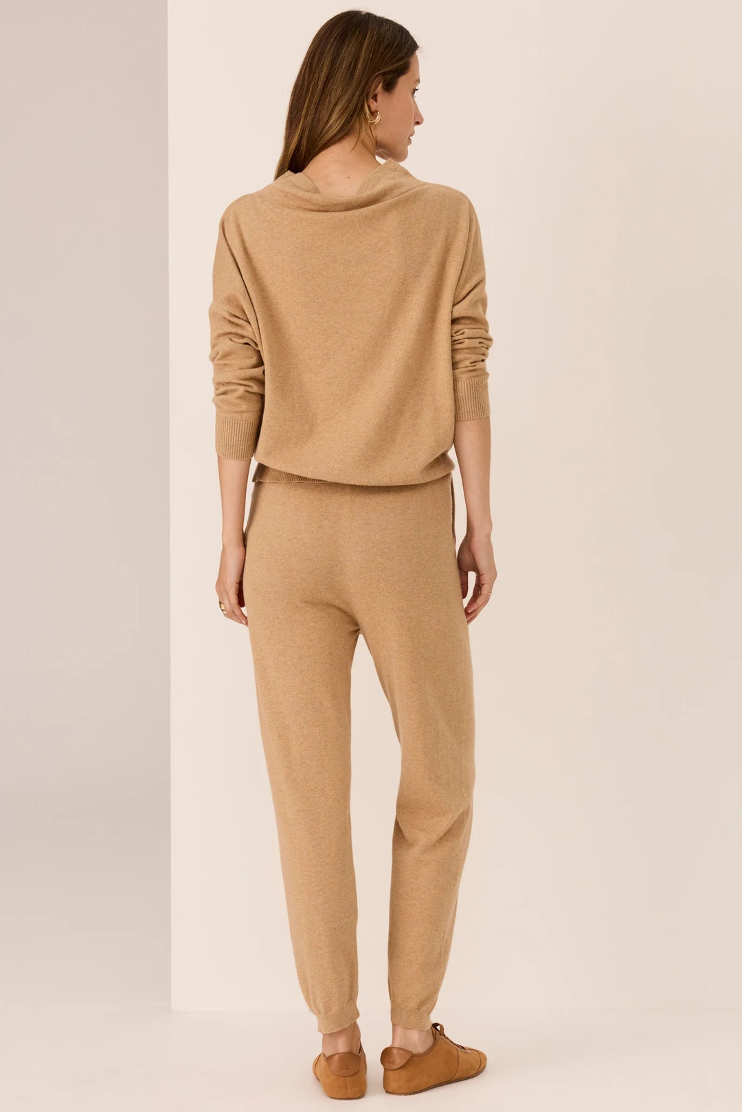 Woman wearing a beige sweater and pants on a plain background