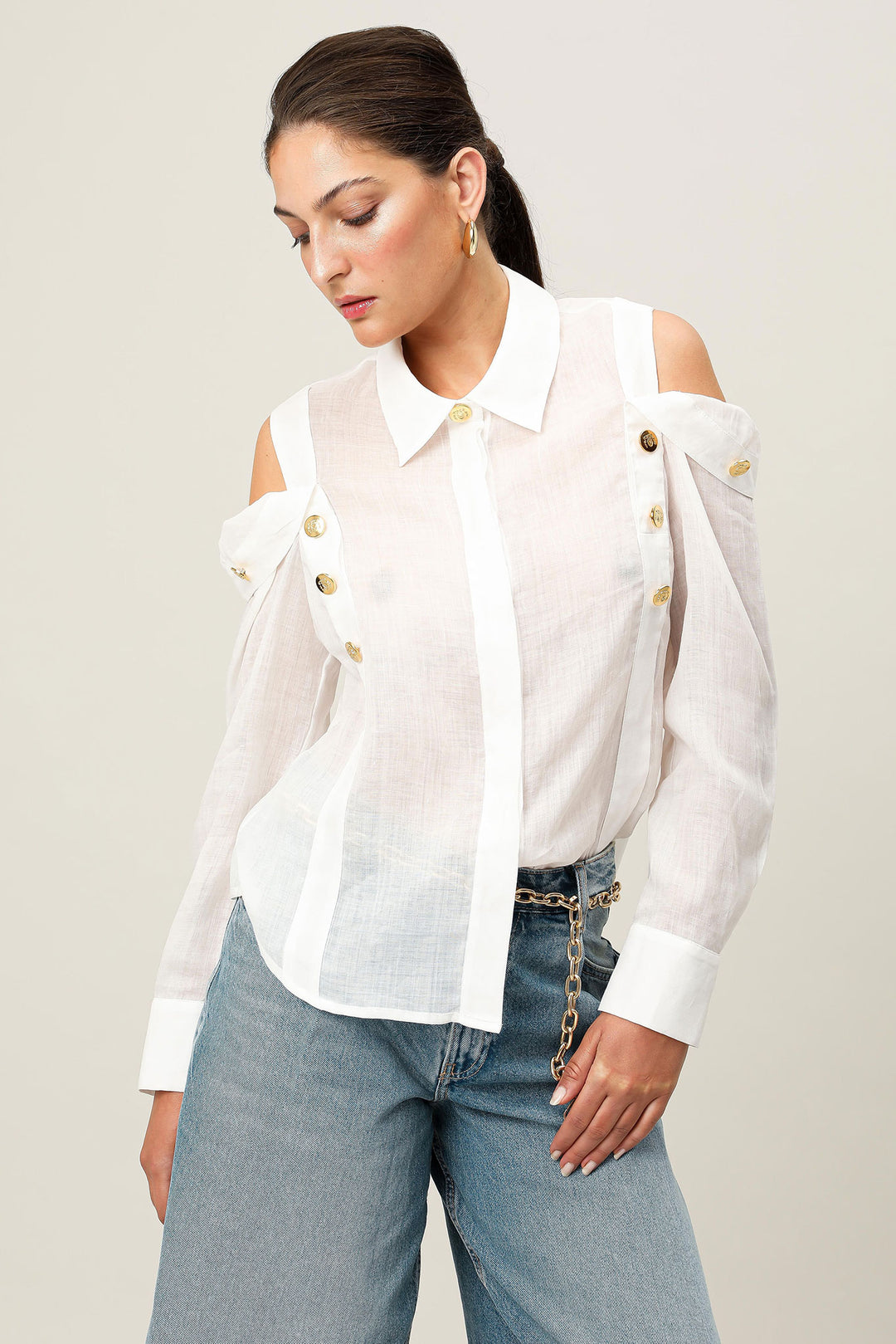 Woman wearing a white blouse with gold buttons and blue jeans on a plain background