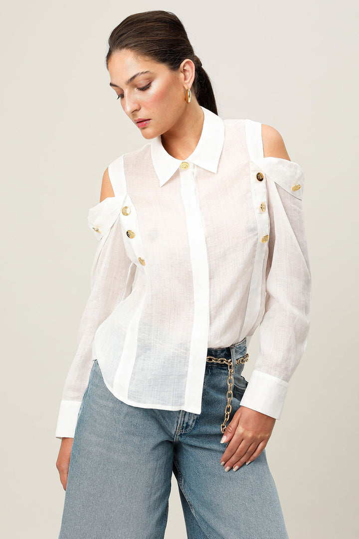 Woman wearing a white blouse with gold buttons and blue jeans on a plain background