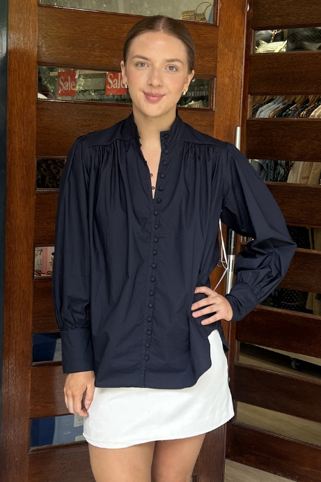 Woman standing in front of a store entrance wearing a navy top and white shorts.