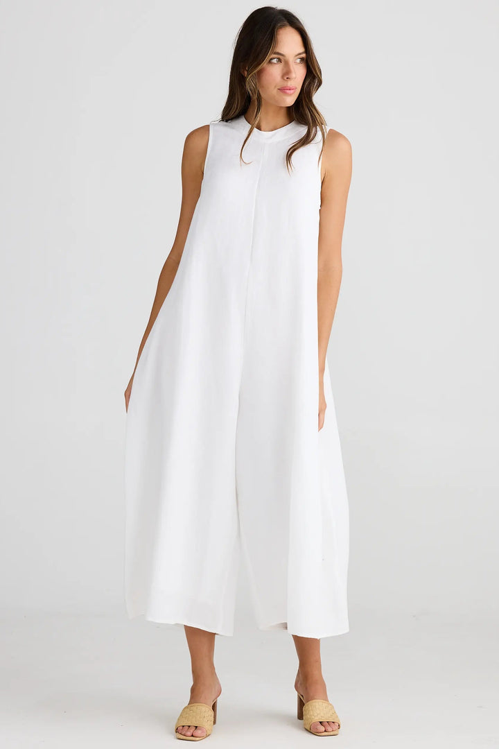 A female model wearing a white pantsuit with a high, round neckline and wide-leg style. The model has her hands at her sides and is posing against a neutral background.