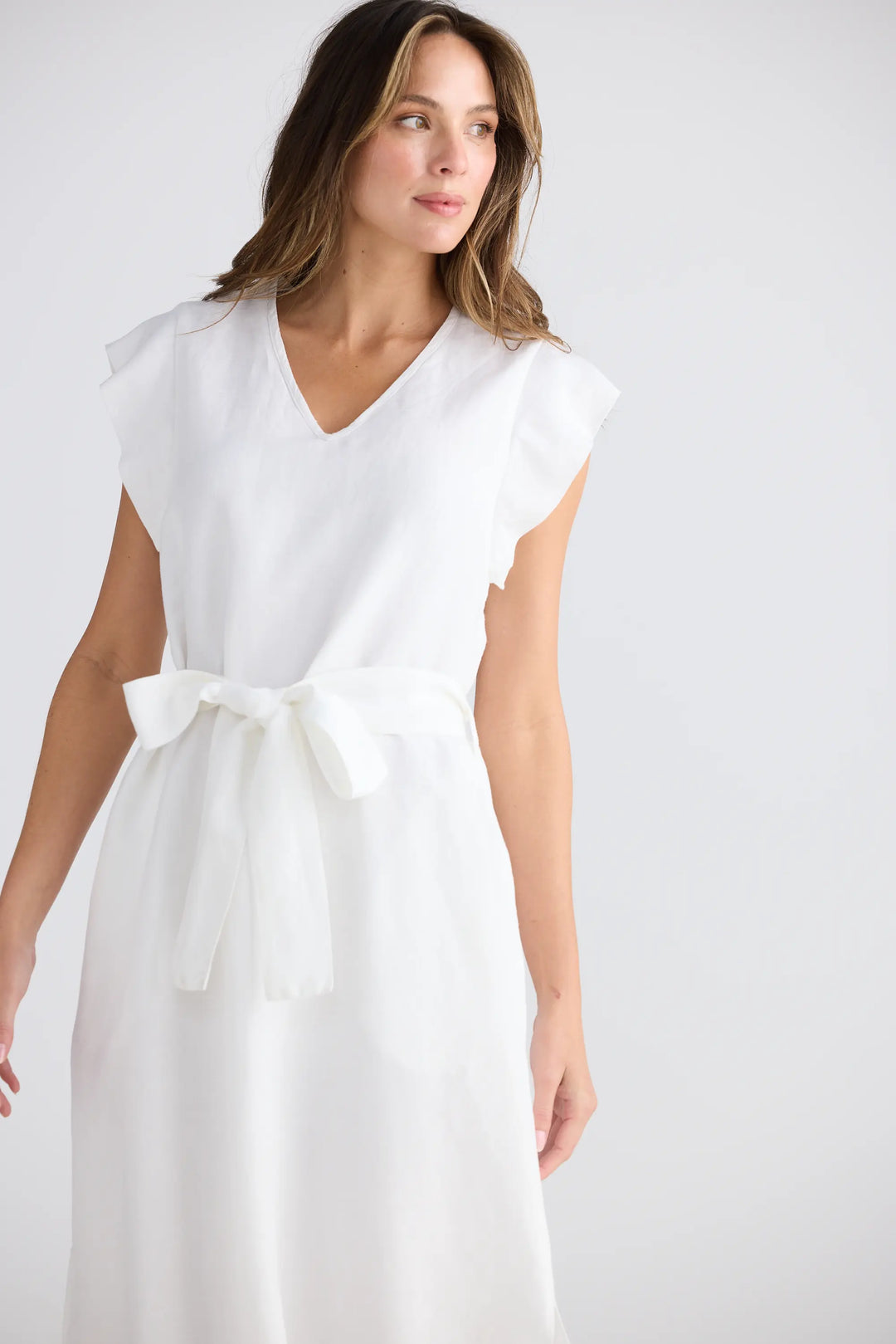 Woman wearing a white dress with a belt on a plain background