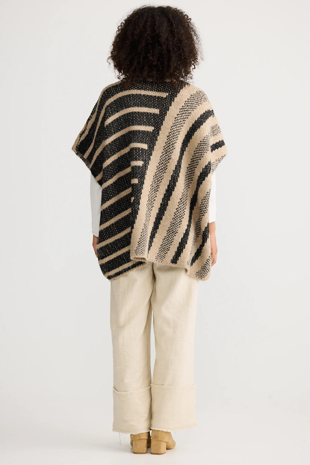 Person wearing a striped poncho and beige pants on a white background