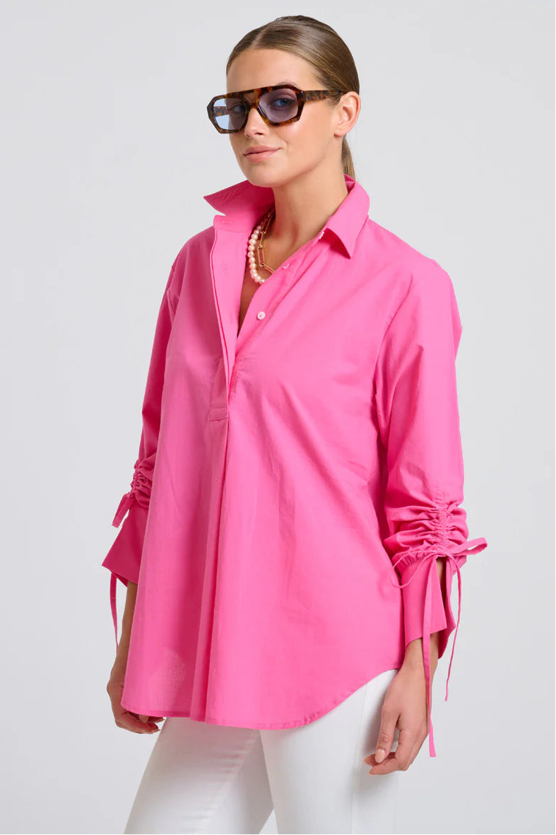 Woman wearing a bright pink shirt with rolled-up sleeves on a white background