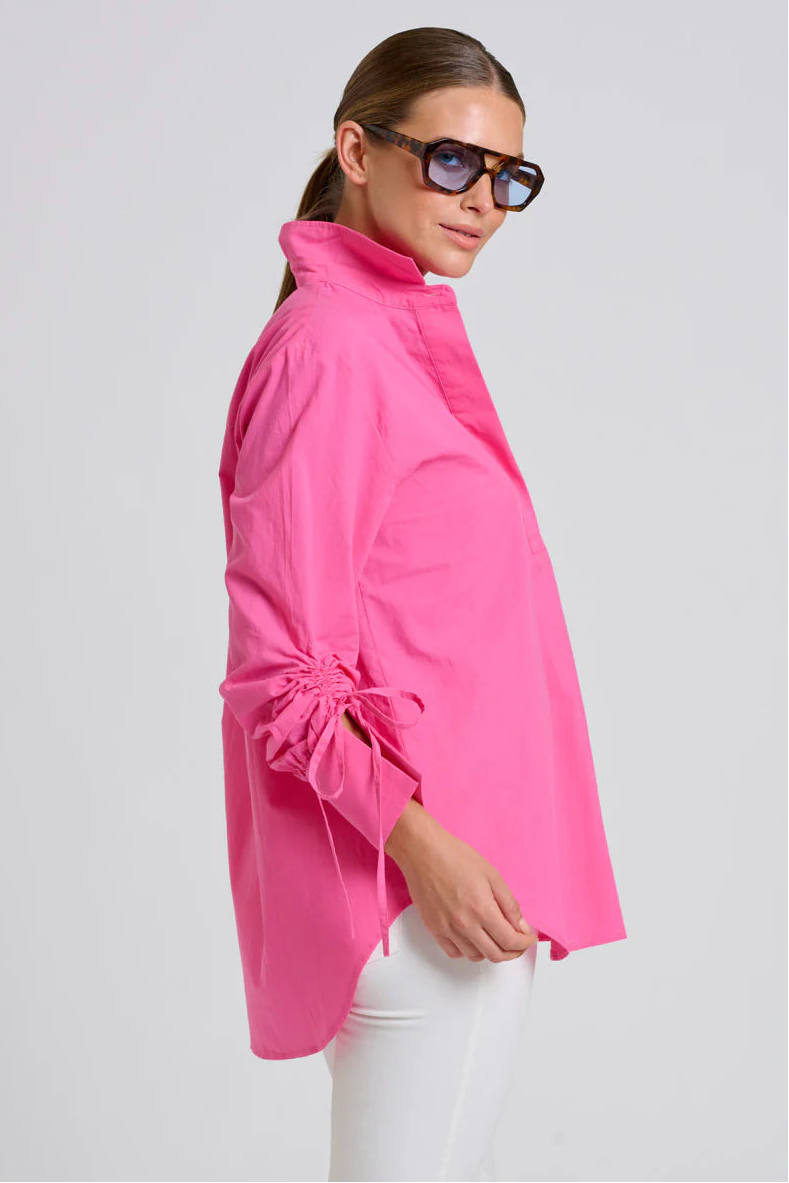Woman wearing a bright pink jacket and sunglasses on a light gray background