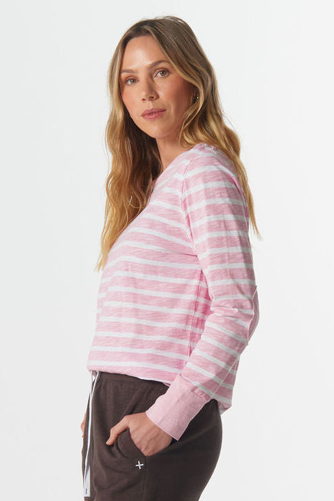 Woman wearing a pink striped sweater and dark pants on a white background