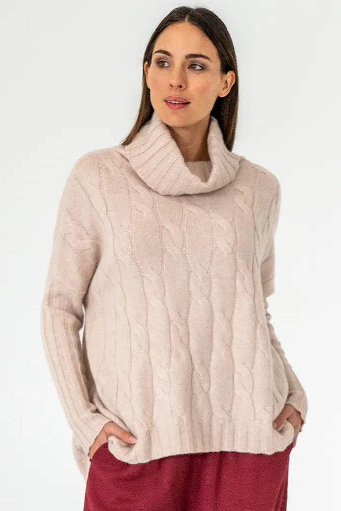 A woman wearing a blush pink cable knit sweater with a turtleneck.