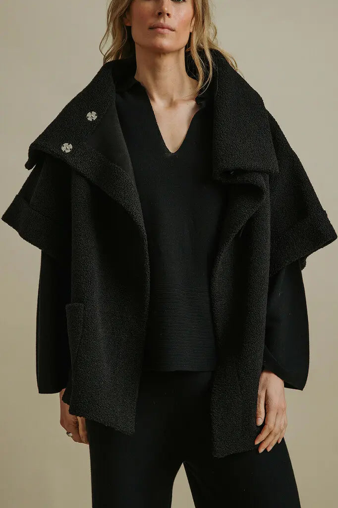 Person wearing a black coat over a plain background
