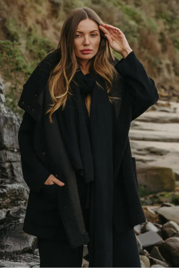 Woman in a black coat standing on a rocky coastal path