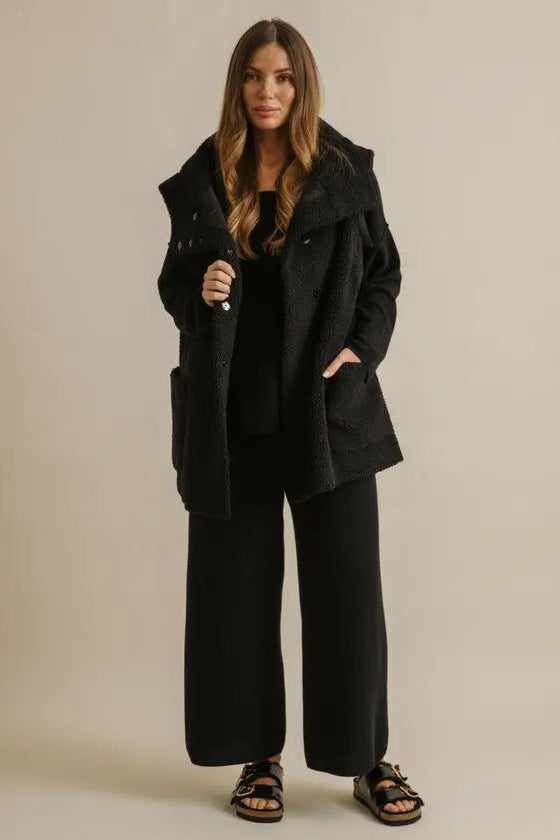 Woman wearing a black coat and pants on a beige background