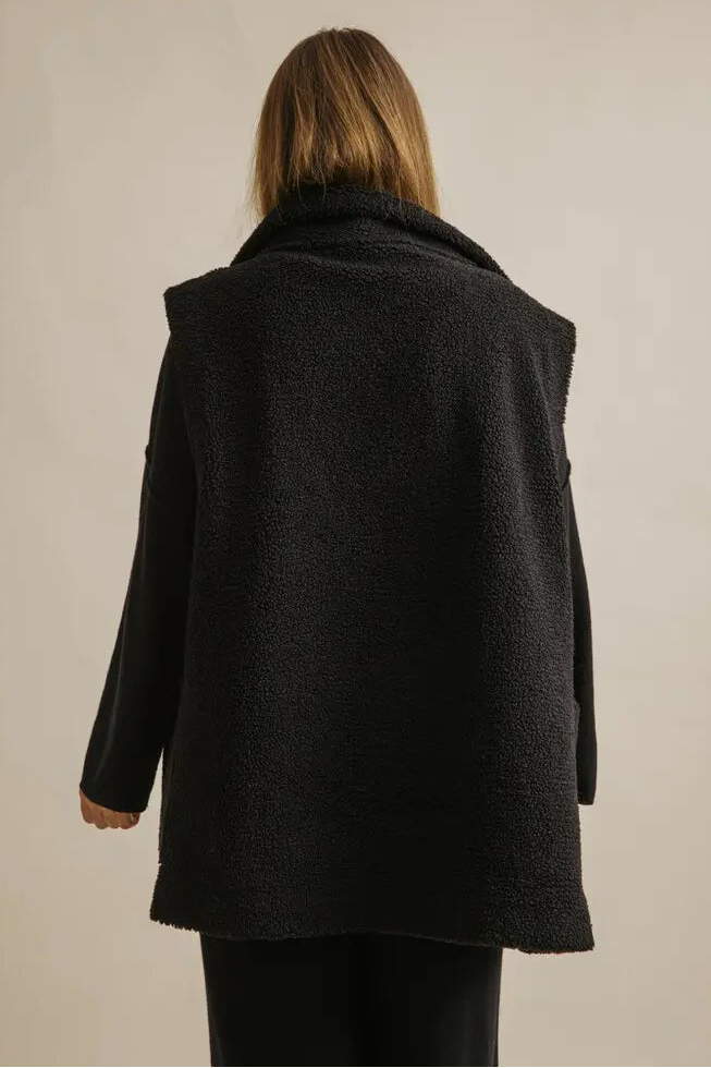 Person wearing a black coat from behind on a plain background