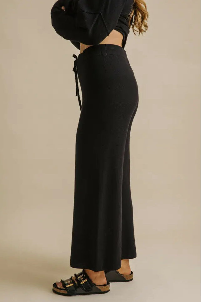 Person wearing black wide-leg pants and a black top on a beige background