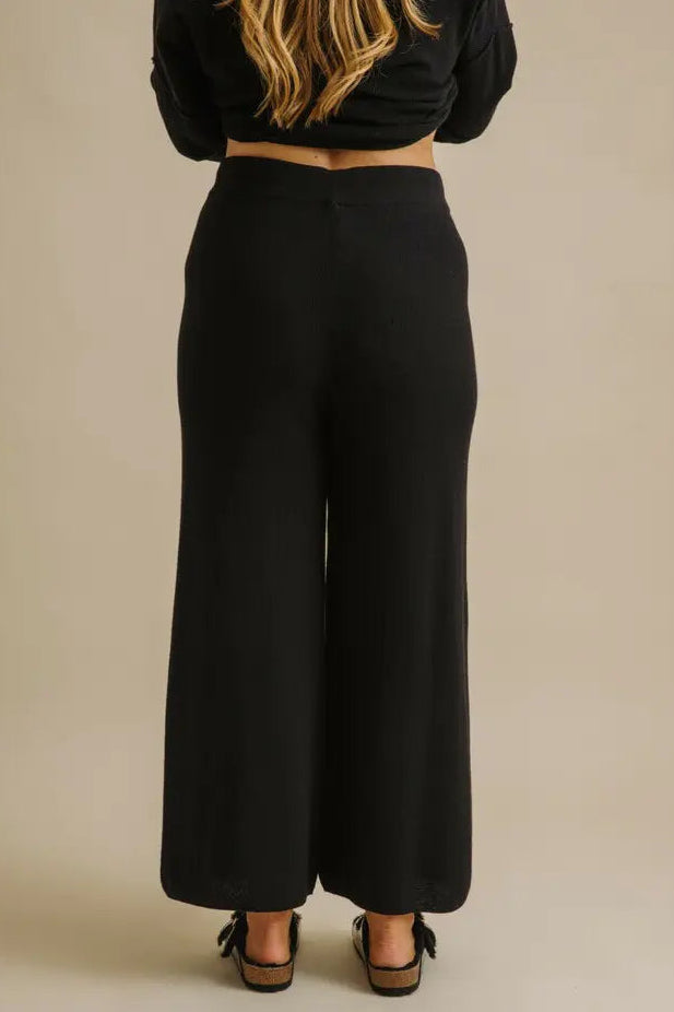 Person wearing black wide-leg pants and a black top on a beige background