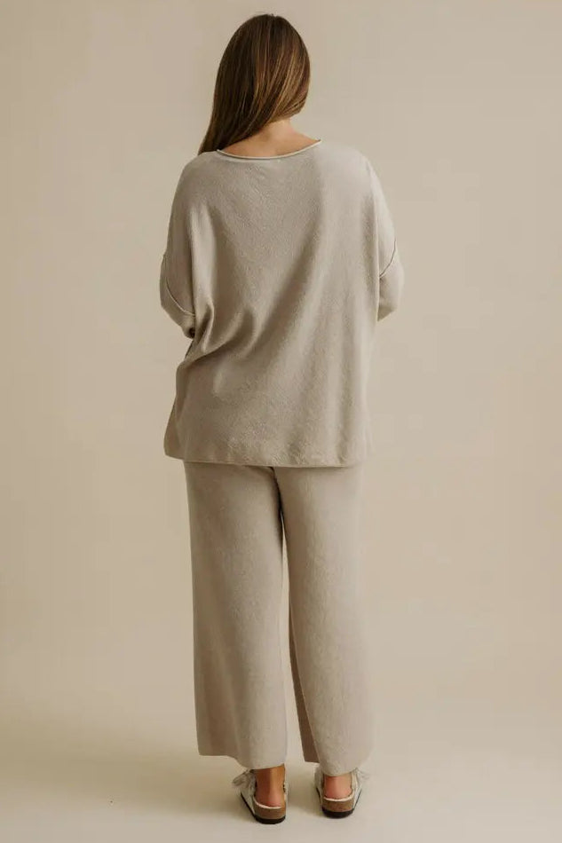 Person wearing a beige outfit standing against a plain background