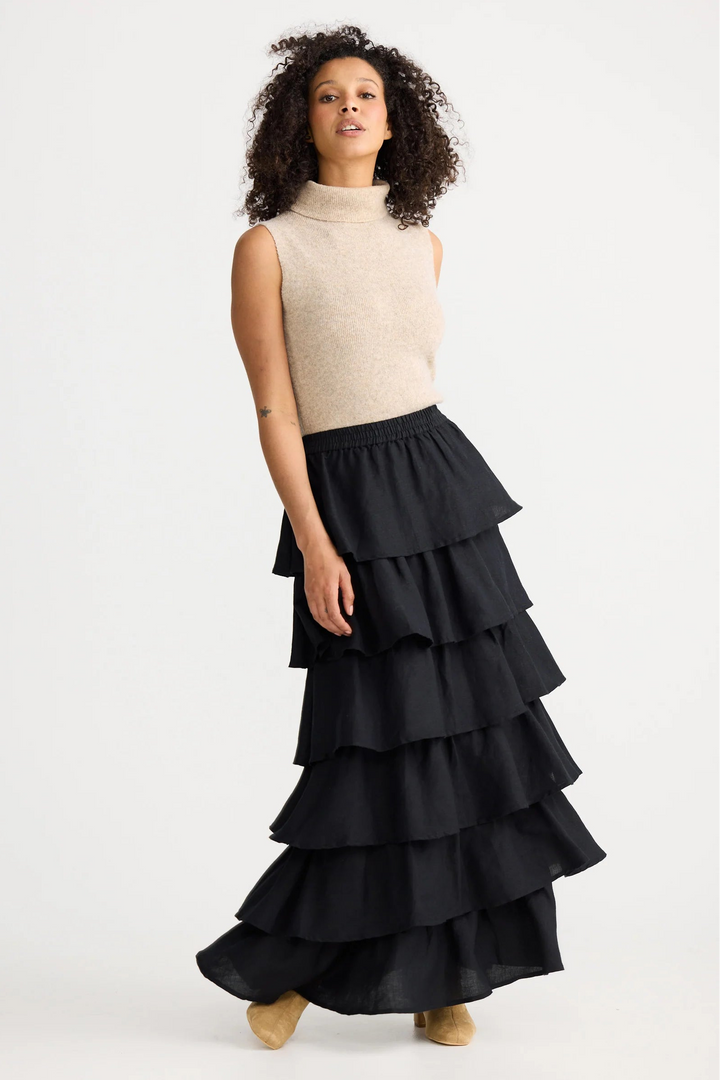 Woman wearing a beige sleeveless sweater and black tiered skirt on a white background