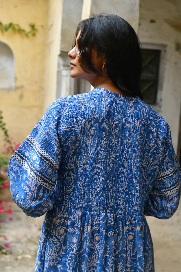 Woman wearing a blue patterned dress standing in front of an old building.
