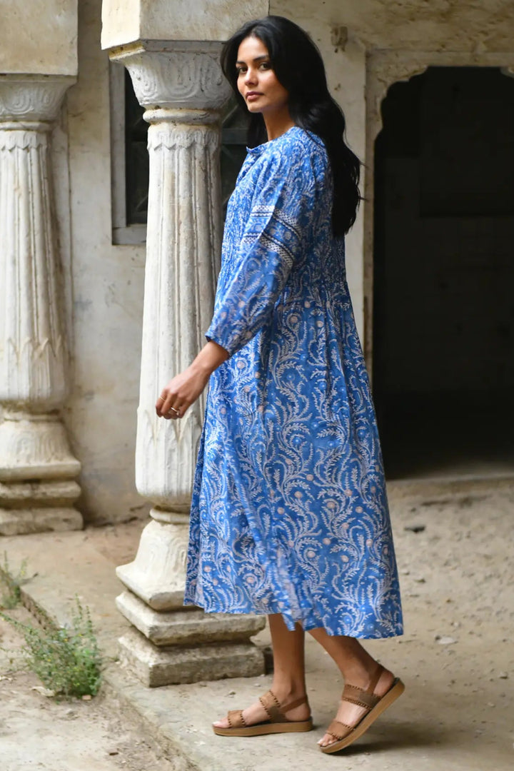 Woman in a blue patterned dress standing in an outdoor setting with columns.