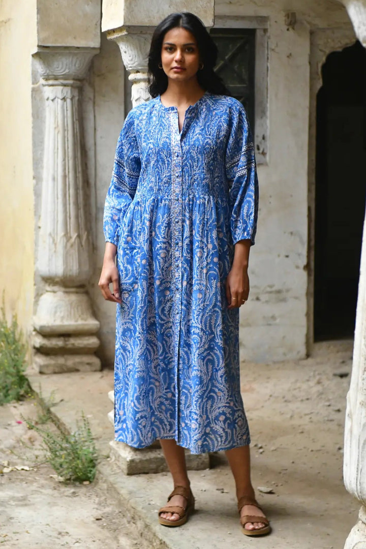 Woman wearing a blue patterned dress standing in an outdoor setting with stone architecture.