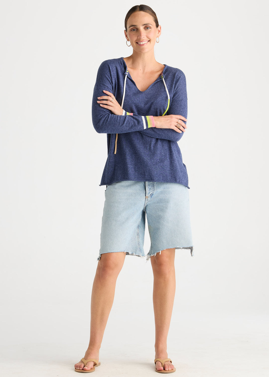 A woman modeling a navy blue long-sleeve knit top with white drawstrings and light-wash denim shorts against a plain white studio background.