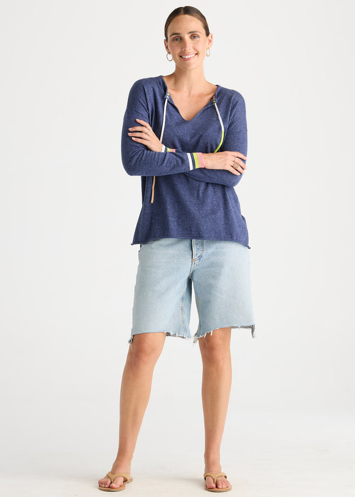 A woman modeling a navy blue long-sleeve knit top with white drawstrings and light-wash denim shorts against a plain white studio background.