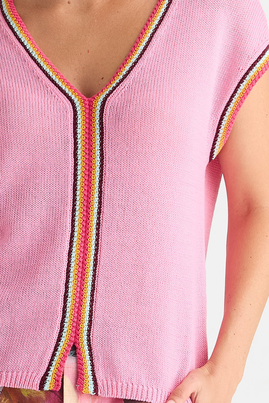 A close-up of a pink knit top with a V-neck and short sleeves, featuring a colorful striped trim in yellow, orange, pink, white, and black.