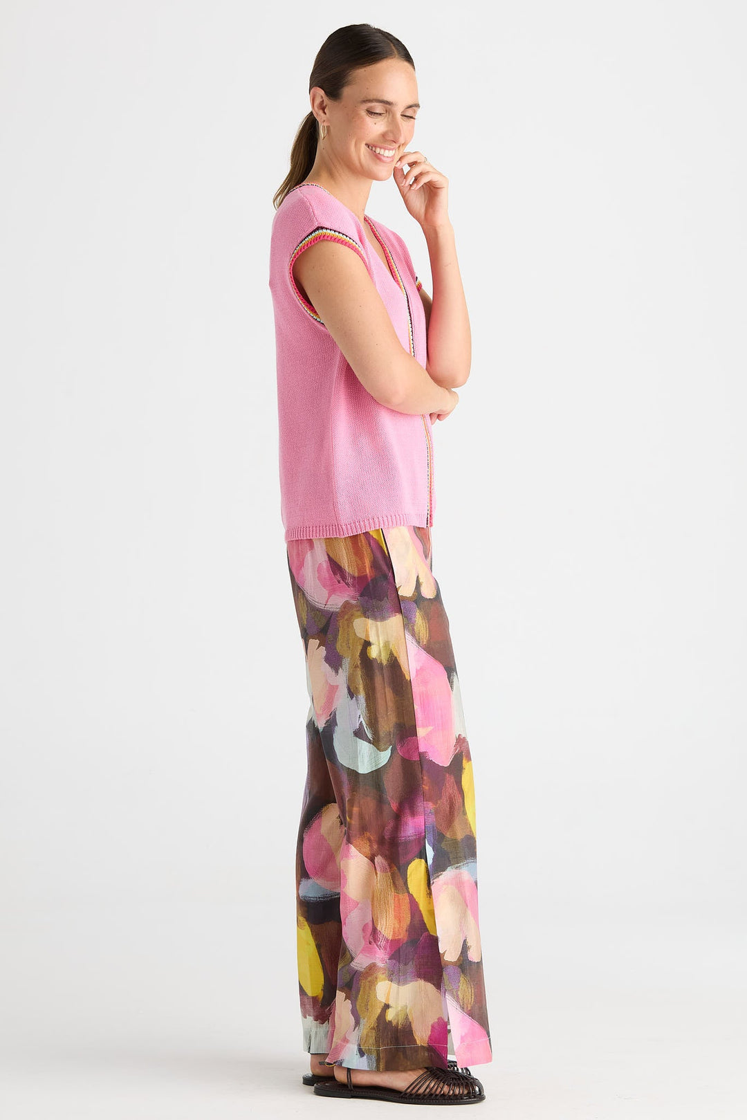 A woman modeling a pink sleeveless knit top paired with wide-leg pants featuring a colorful abstract floral print, photographed against a plain light gray studio background.