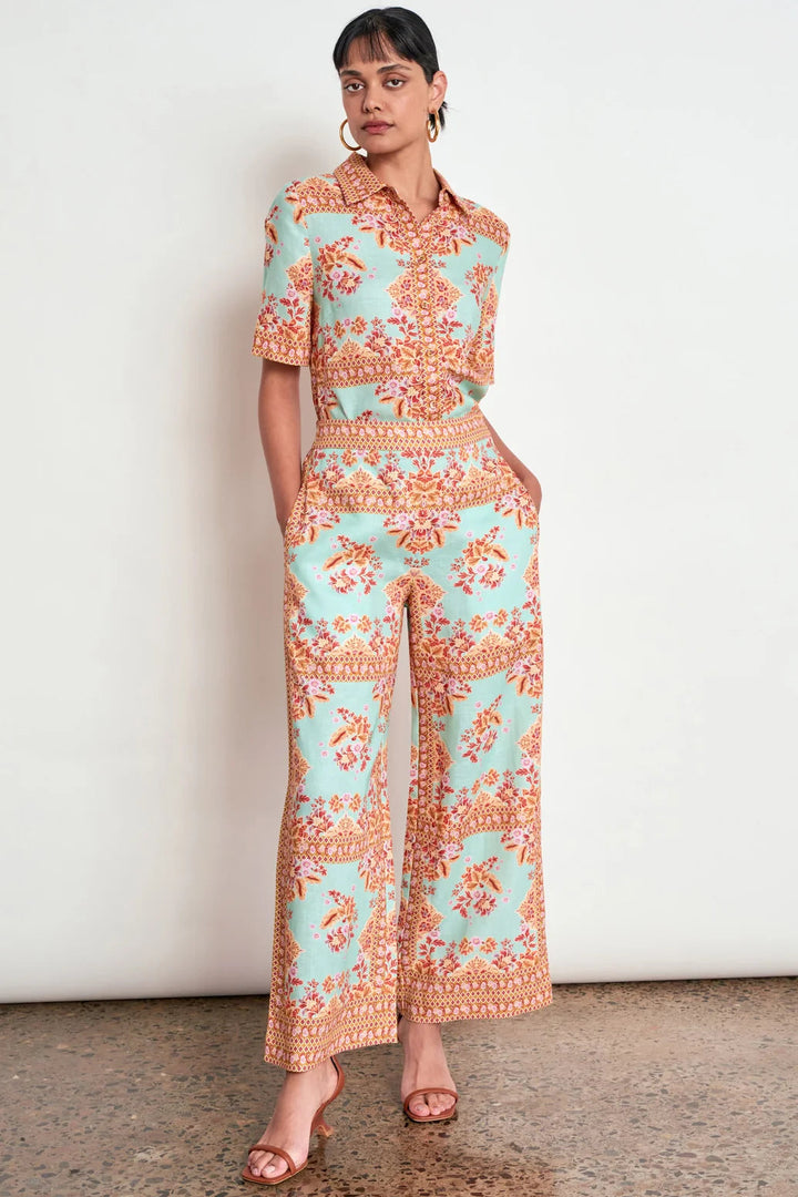 A woman models a matching short-sleeve collared top and wide-leg cropped pants set in a mint green and orange paisley pattern, standing against a white wall.