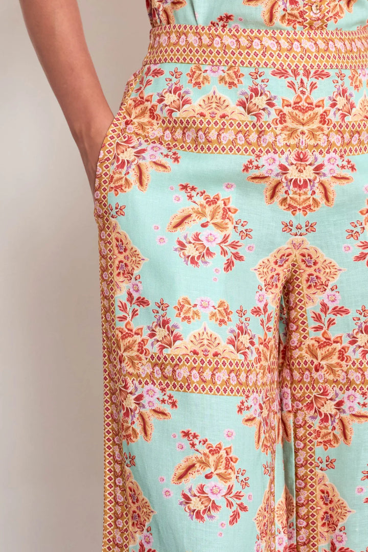 A close-up of a model wearing a light mint green skirt with a detailed orange, pink, and gold floral and geometric pattern.