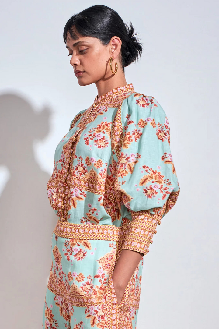 A woman wearing a light mint green and orange floral print dress with patterned trim, shown in a side profile against a plain light gray background.