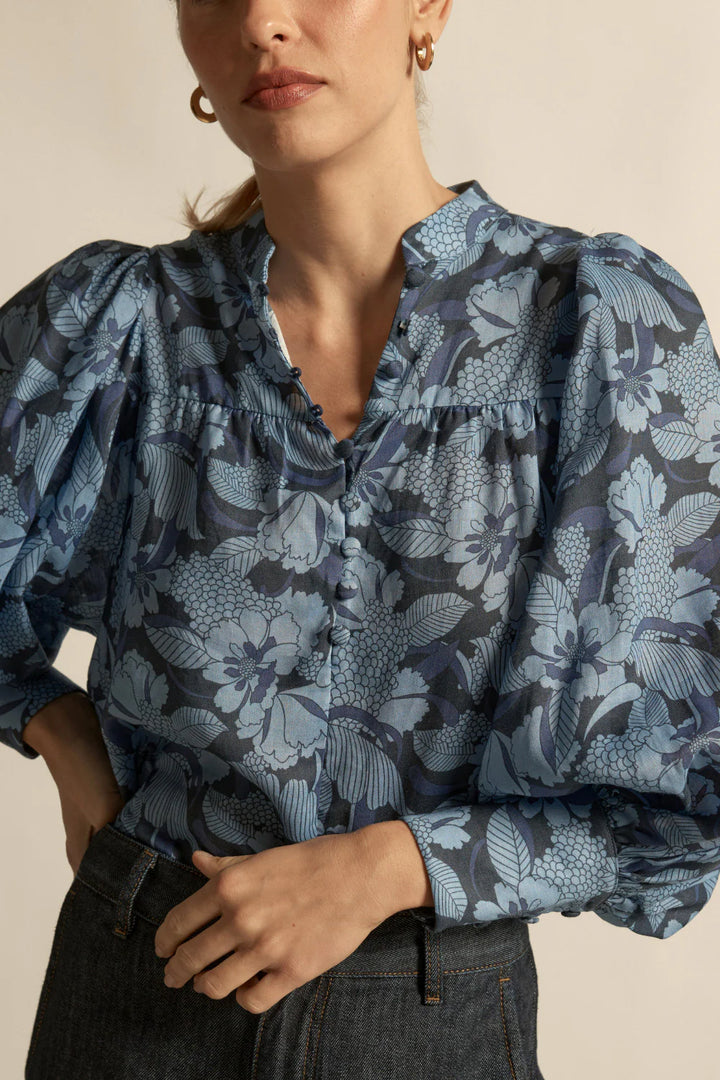 Woman wearing a blue floral blouse with puffed sleeves against a beige background