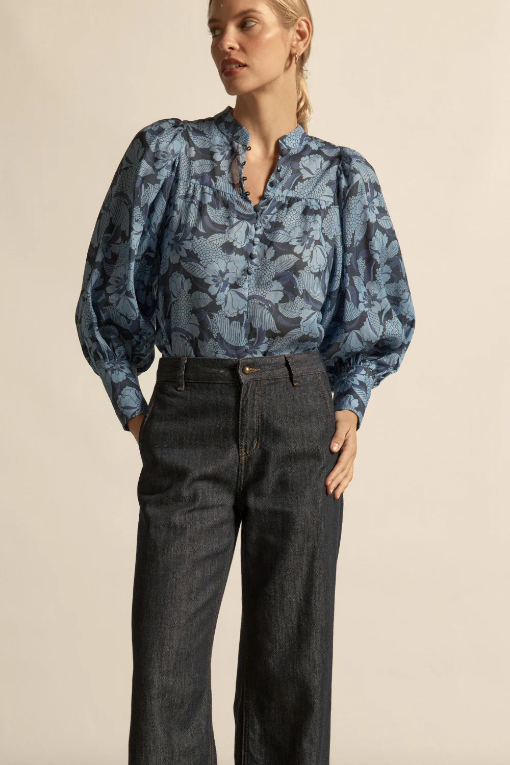 Woman wearing a blue floral blouse and dark jeans against a beige background