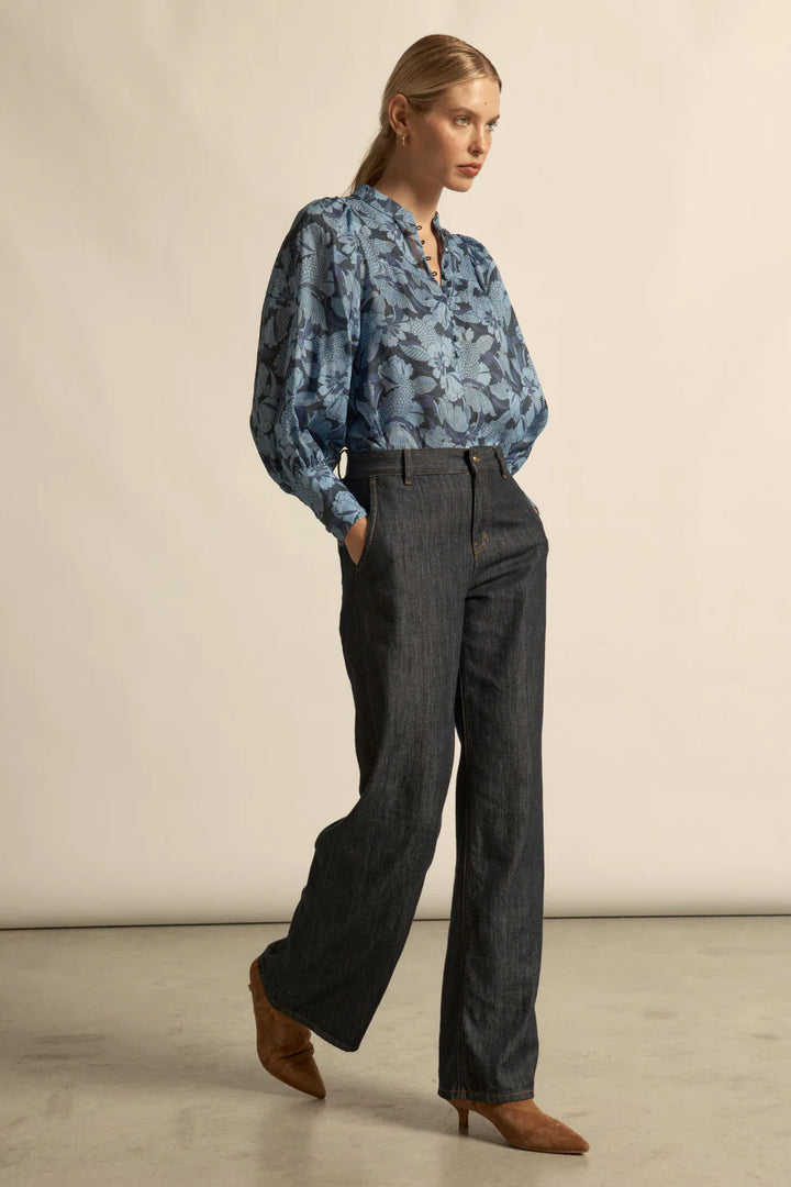 Woman wearing a blue floral blouse and dark pants against a plain background