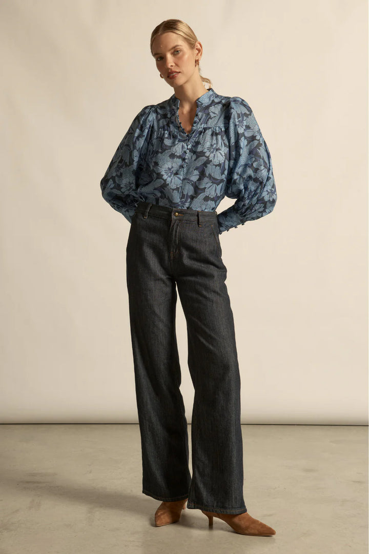 Woman wearing a blue floral blouse and dark jeans against a neutral background