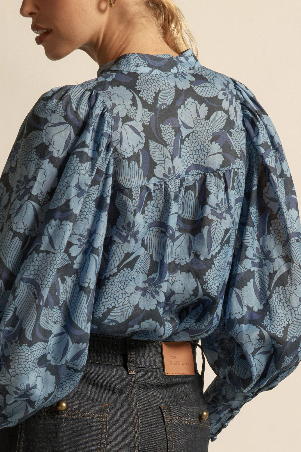 Person wearing a blue floral patterned blouse with puffed sleeves on a beige background