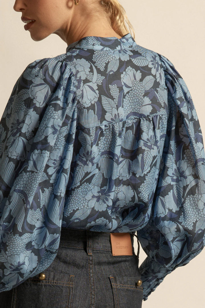 Person wearing a blue floral patterned blouse with puffed sleeves on a beige background