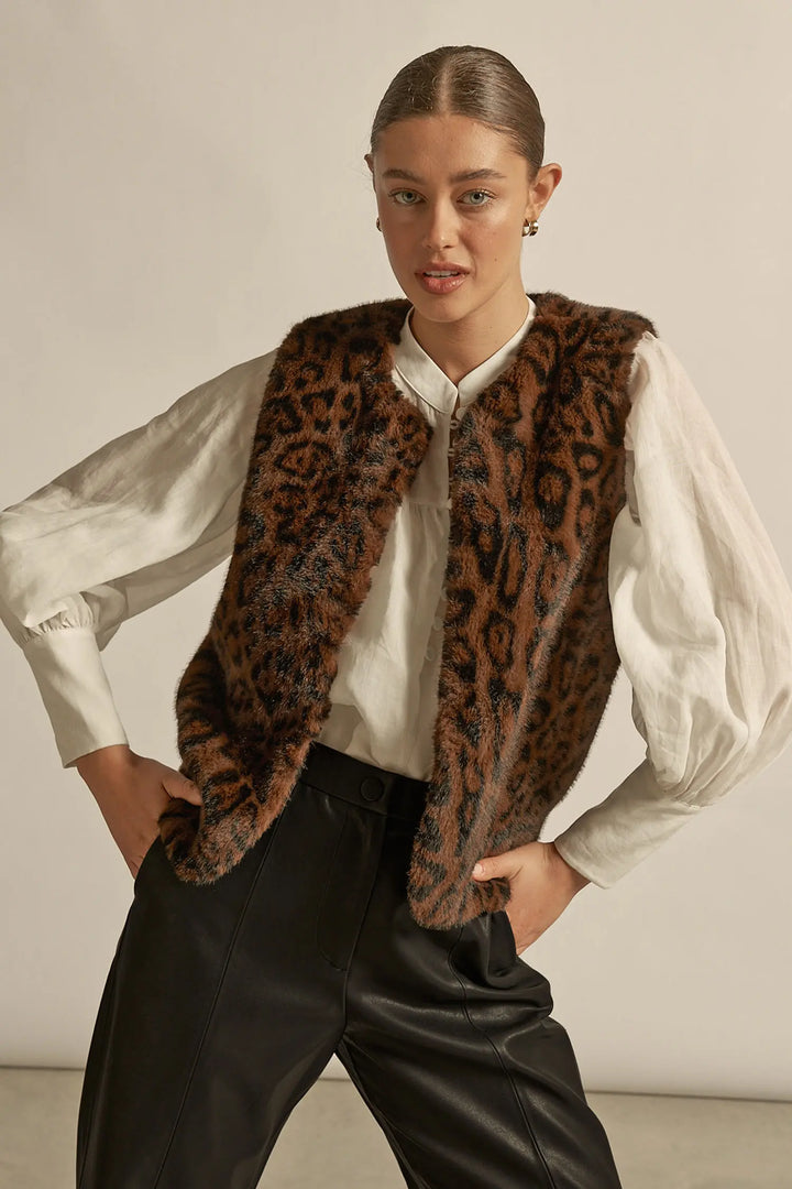 Person wearing a leopard print vest over a white shirt with a neutral background