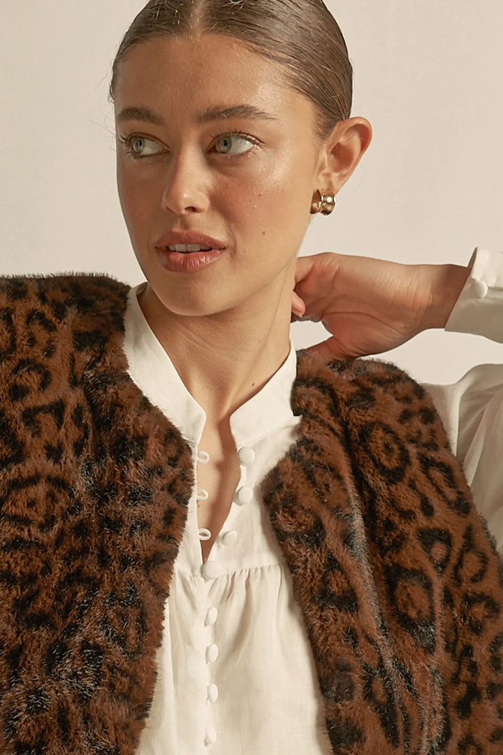 Person wearing a leopard print vest over a white shirt with a neutral background
