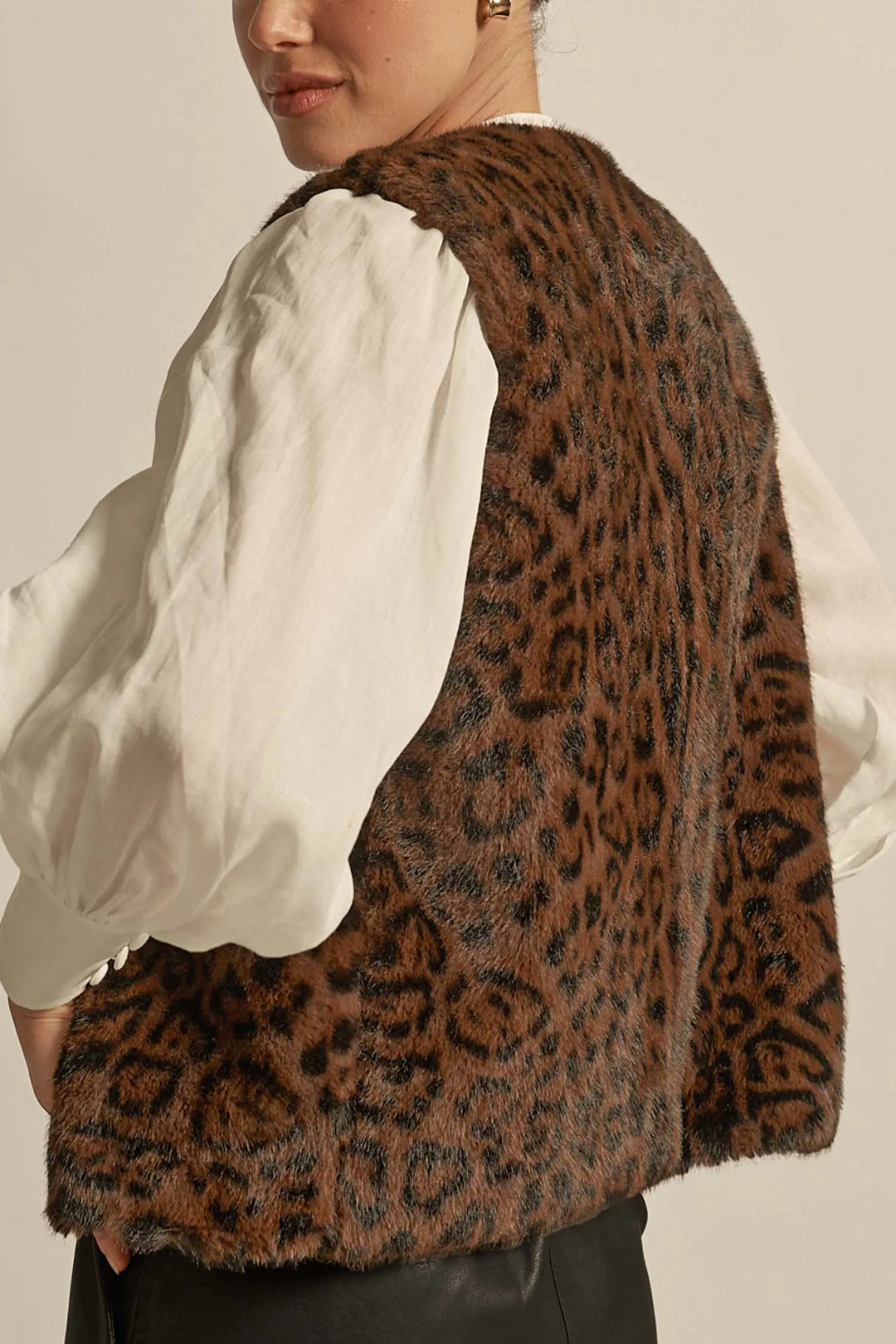 Person wearing a leopard print vest over a white shirt on a neutral background