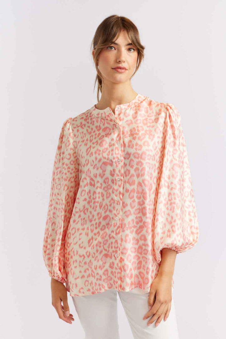 A woman wearing a pink silk shirt with a classic animal print and a mandarin collar, paired with white pants.