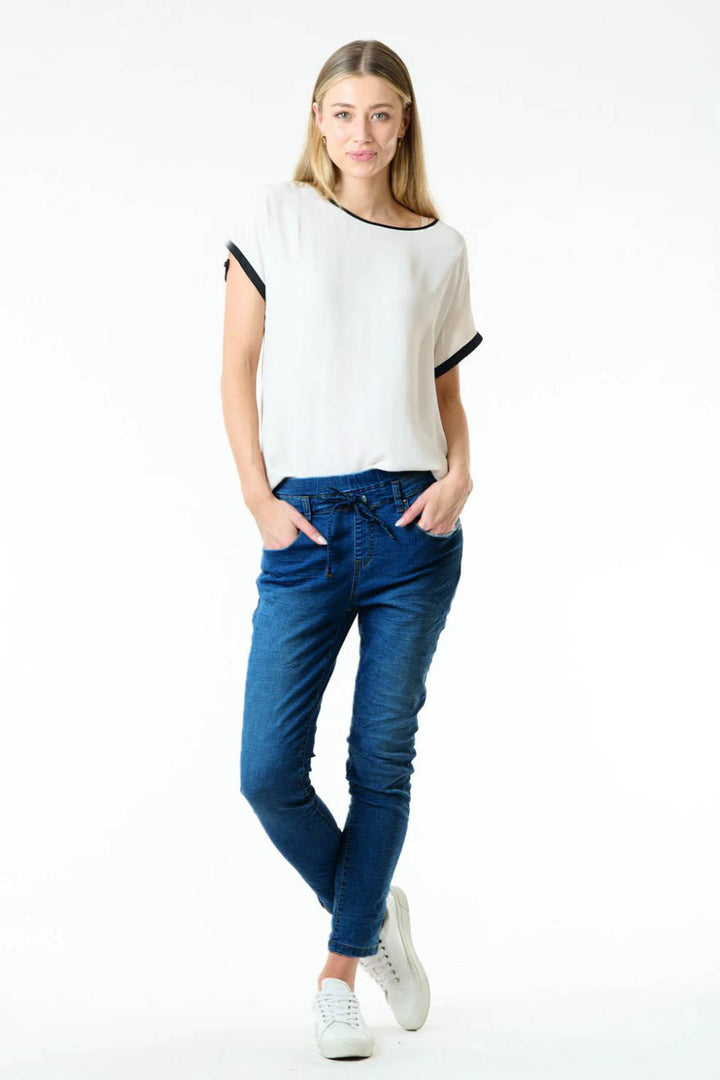 A female model wearing a white top with black trim and blue relaxed jogger jeans with an adjustable tie waist.