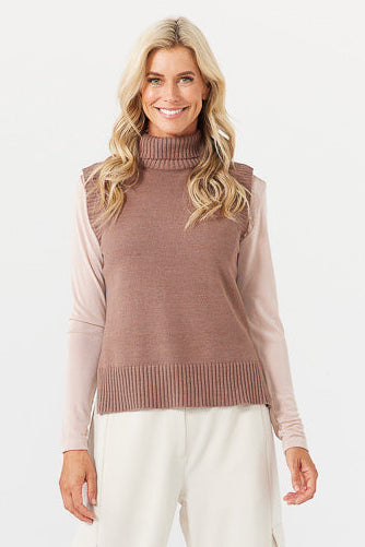 Woman wearing a brown ribbed sweater over a pink long-sleeve shirt on a white background