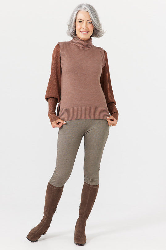 Woman wearing a brown turtleneck sweater, beige leggings, and brown knee-high boots on a white background