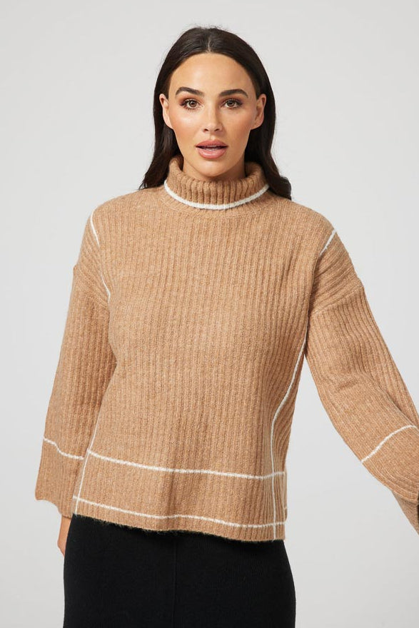 A female model wearing a tan colored knit sweater with a high neck, flared sleeves, and contrast yarn details.